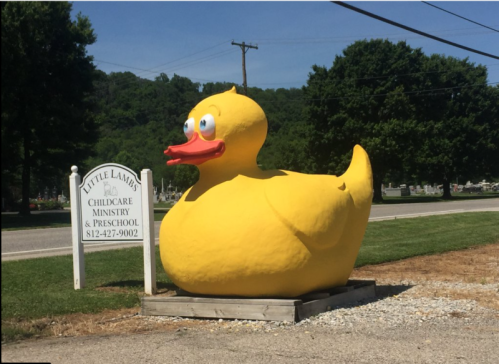 A large, bright yellow rubber duck statue outside Little Lambs Childcare Ministry and Preschool.