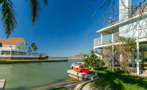 A serene waterfront scene featuring a canal, colorful kayaks, and a charming house under a clear blue sky.