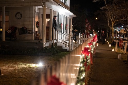 A festive night scene with a decorated house, lit pathway, and people enjoying the holiday atmosphere.