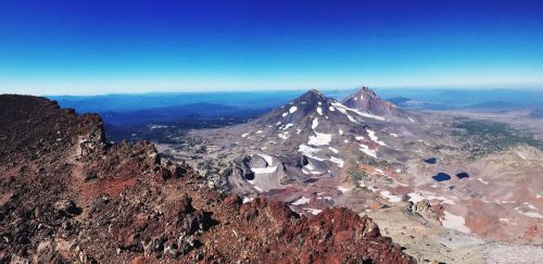 A panoramic view of rugged mountains with snow-capped peaks under a clear blue sky.