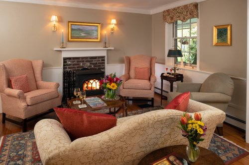 Cozy living room with a fireplace, two armchairs, a sofa, and a coffee table adorned with flowers and drinks.