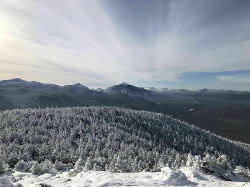 A panoramic view of snow-covered mountains and forests under a cloudy sky.