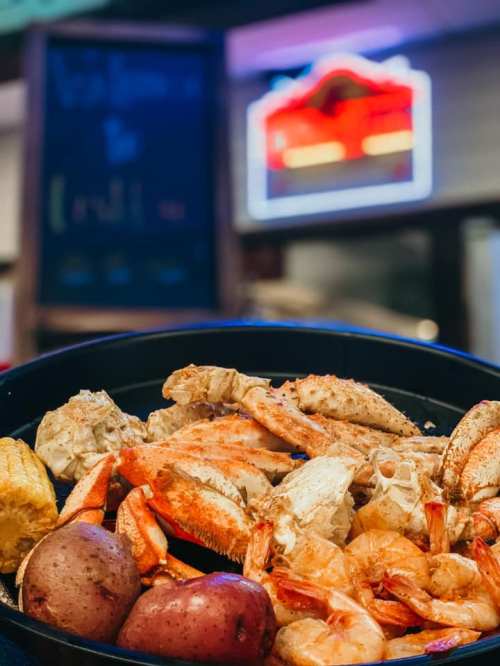 A platter of seafood featuring crabs, shrimp, and potatoes, with a neon sign in the background.