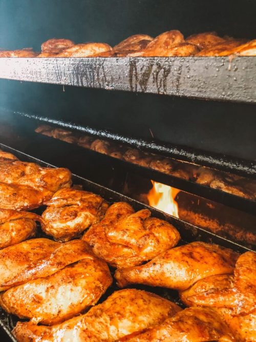 Smoky barbecue chicken cooking on racks in a smoker, with flames visible in the background.