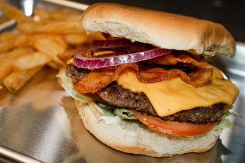 A juicy cheeseburger with bacon, lettuce, tomato, and red onion, served with crispy fries on the side.