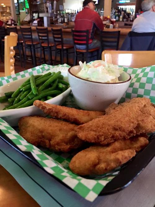 A plate of fried fish fillets with green beans and coleslaw, served in a basket with a checkered liner.