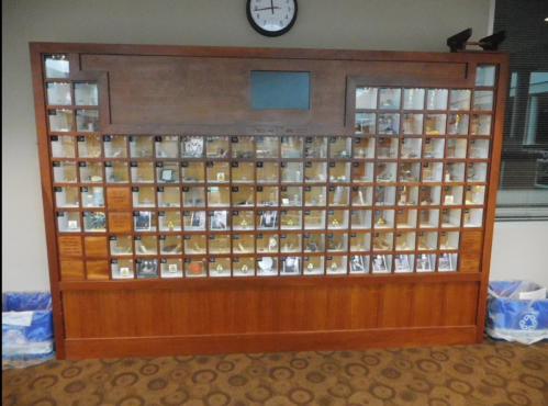 Display case with numerous small compartments showcasing various items and photographs, set against a wooden background.