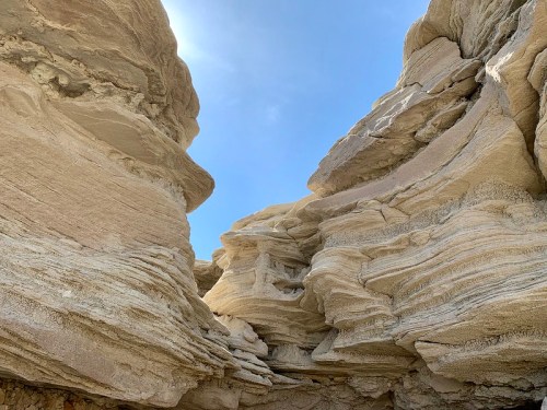 A narrow canyon with layered rock formations under a clear blue sky.