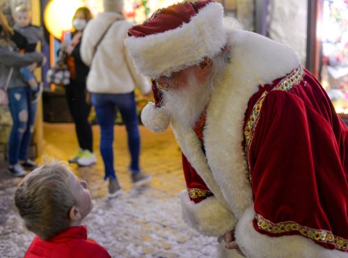 A child looks up at Santa Claus, who is wearing a red suit and white beard, in a festive holiday setting.
