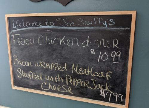 Chalkboard menu at Joe Snuffy's featuring fried chicken dinner and bacon-wrapped meatloaf with pepper jack cheese.