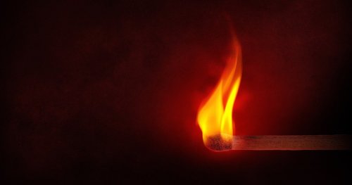 A lit matchstick with a bright flame against a dark background.