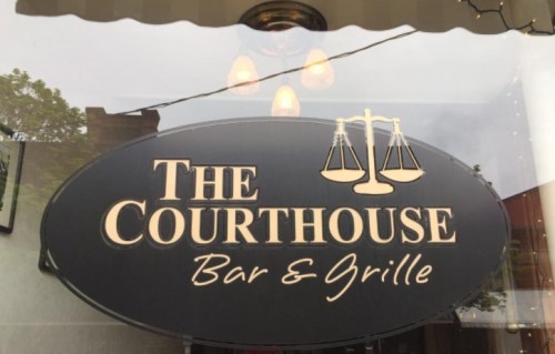 Sign for "The Courthouse Bar & Grille" featuring scales of justice, hanging under a light fixture.