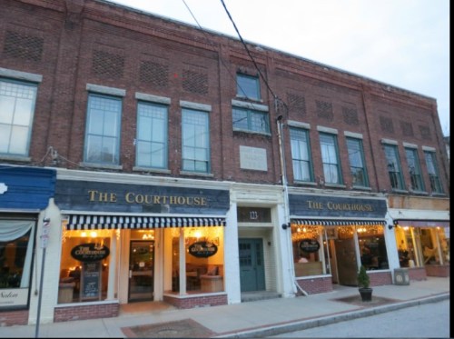 Historic brick building with large windows, featuring "The Courthouse" signage and warm lights in the windows.