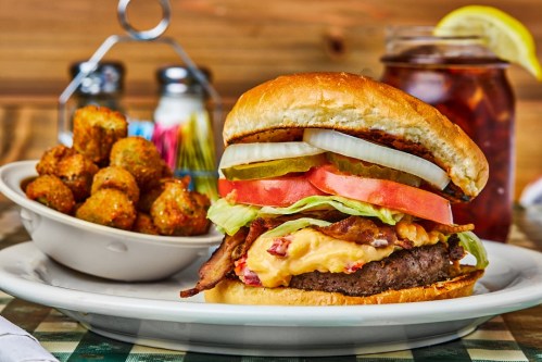 A juicy burger with bacon, cheese, lettuce, tomato, and pickles, served with a side of crispy tater tots and iced tea.