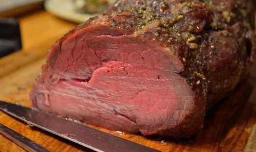 A close-up of a perfectly cooked roast beef, sliced to reveal its pink, juicy interior, resting on a wooden cutting board.