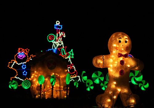 A glowing gingerbread man stands in front of a brightly lit candy-themed house and colorful candy decorations.