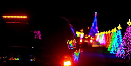 A car parked on a road lined with colorful holiday lights, creating a festive nighttime scene.