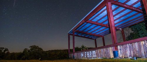 A red barn structure under a starry night sky, with trees in the background and a clear view of the stars.