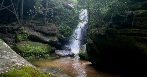 A serene waterfall cascades through lush greenery and rocky formations, creating a tranquil natural scene.
