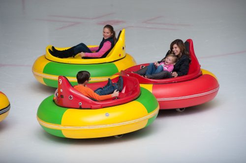 Four people enjoy bumper cars on ice, smiling and having fun in colorful inflatable vehicles.