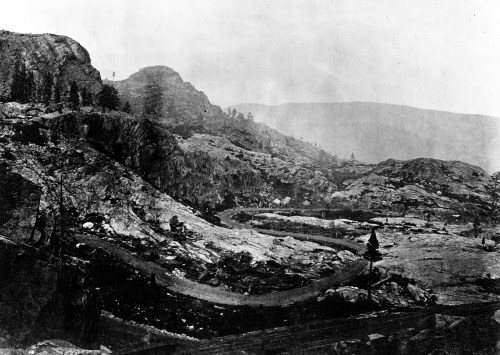 A black and white landscape featuring rocky terrain, hills, and a winding path through a mountainous area.