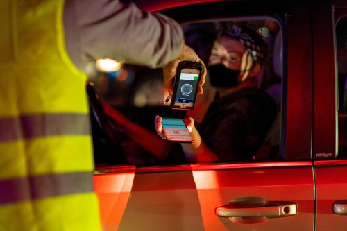 A person in a car shows their phone to a person in a reflective vest during a nighttime check.