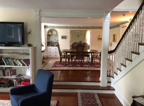 A cozy living space featuring a staircase, dining area, and bookshelves, with warm lighting and decorative elements.