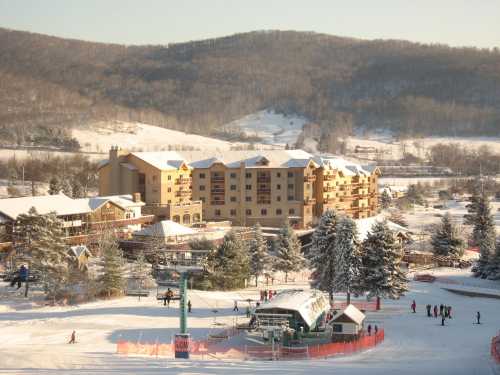 A snowy landscape featuring a ski resort with a lodge, trees, and people enjoying winter activities.