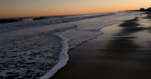 A serene beach at sunset, with gentle waves lapping at the shore and a colorful sky reflecting on the water.