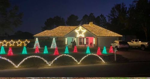 A house decorated with colorful Christmas lights, featuring a star on the roof and illuminated trees in the yard.