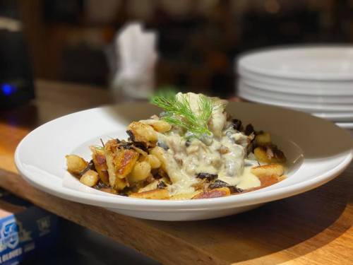 A plate of sautéed potatoes topped with a creamy sauce and garnished with a sprig of dill.