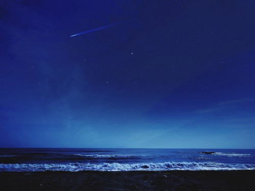 A serene night scene of a dark ocean under a starry sky, with a comet streaking across the horizon.