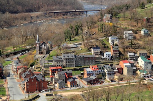 Aerial view of a small town with historic buildings, a river, and a bridge in the background, surrounded by trees.