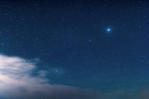 A clear night sky filled with stars, featuring a bright planet and wispy clouds at the bottom.