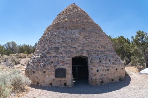 A stone beehive-shaped kiln surrounded by desert vegetation under a clear blue sky.
