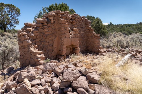 Ruins of a stone structure surrounded by rocky terrain and sparse vegetation under a clear blue sky.