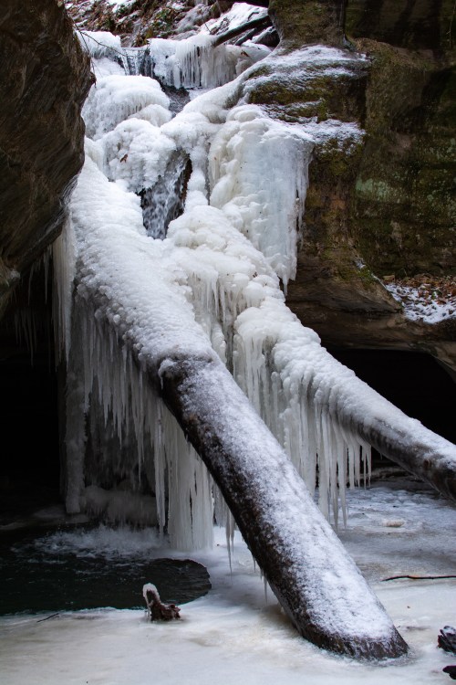 A frozen waterfall with icicles hanging from rocks and a snowy landscape below.