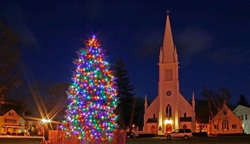 A brightly lit Christmas tree stands in front of a church at night, creating a festive holiday scene.