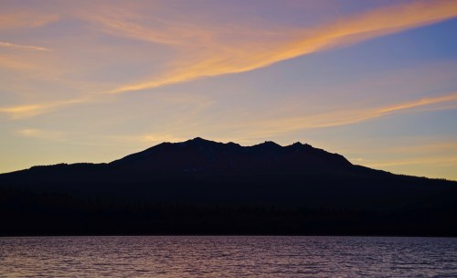 Silhouette of a mountain against a colorful sunset sky, reflected in a calm lake.