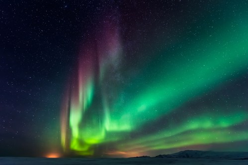 A vibrant display of the Northern Lights illuminates the night sky with green and purple hues over a snowy landscape.