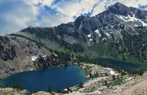 A scenic view of two blue lakes surrounded by green hills and rugged mountains under a partly cloudy sky.