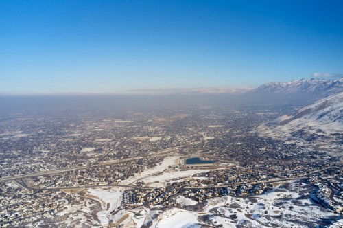Aerial view of a snowy landscape with a city, mountains, and a clear blue sky in the background.