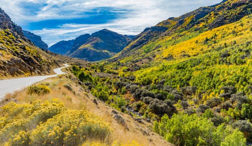 A winding road through a vibrant valley surrounded by mountains and colorful autumn foliage.