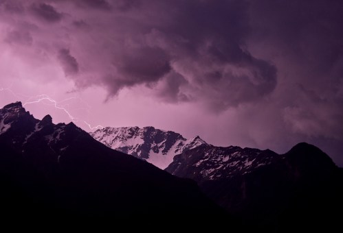 Dramatic mountain landscape under a stormy sky, illuminated by lightning and shrouded in dark clouds.