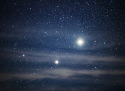 A starry night sky with bright celestial bodies and faint clouds, creating a serene cosmic scene.