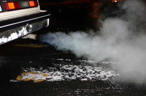 Exhaust pipe emitting white smoke on a wet surface, with snow-like residue nearby.