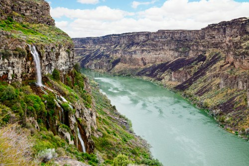 A scenic view of a river winding through rocky cliffs, with waterfalls cascading down the lush green landscape.