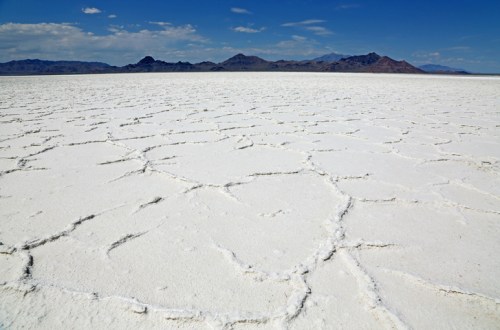 A vast, cracked salt flat stretches under a blue sky with distant mountains in the background.