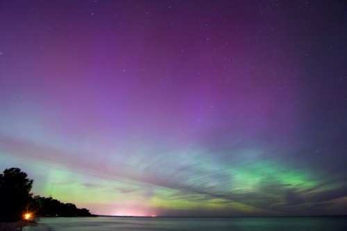 A vibrant night sky filled with purple and green auroras over a calm lake, with stars twinkling above.