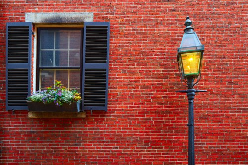 A brick wall with a window featuring flower boxes and a vintage street lamp beside it.